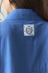Camisa azul de algodón con detalles de ondas rojas en la solapa del cierre y en los puños, de manga larga y corte oversize.