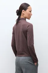 Media polera de manga larga con cuello alto y detalle de frunces en los puños, confeccionada en tejido suave y elástico.