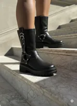 Botas de caña media en cuero negro, con suela track dentada y taco cuadrado. Presentan un diseño con correas ajustables, argollas metálicas y detalles de tachas plateadas.