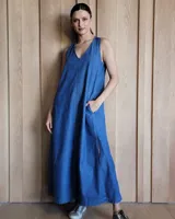 Vestido largo de denim azul, con escote en V, sin mangas, corte holgado, bolsillos laterales y aberturas en los costados de la falda.
