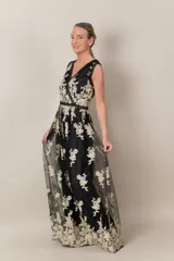 Vestido largo de tul negro con bordado dorado de flores. Tiene escote en V cruzado, sin mangas y falda amplia.