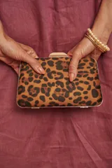 Cartera tipo clutch rígida con estampado animal print de leopardo, marco metálico dorado y cierre superior de broche.