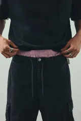 Pantalón cargo negro con efecto lavado, confeccionado en sarga de algodón suave. Presenta cintura elástica con cordón ajustable, cierre de botón a presión, bolsillos laterales, bolsillos cargo con solapa en las piernas y cordón ajustable en el bajo. Corte holgado.