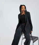 Blazer largo de mujer, color gris oscuro, con rayas verticales finas (riscas de giz). Presenta solapa de muesca, cierre frontal de dos botones y bolsillos de ojal.