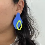 Par de aros colgantes con formas abstractas en azul y amarillo, unidos por una pieza verde.