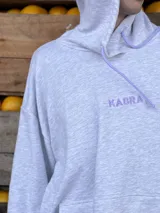 Canguro gris melange con capucha y cordones ajustables en color lila. Presenta el logo bordado en el pecho en color lila y bolsillo frontal tipo canguro.