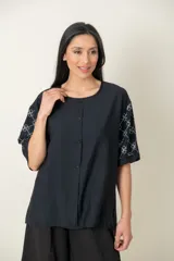 Blusa negra de viscosa con estampado de flores blancas en las mangas, corte holgado, cuello redondo y botones frontales.
