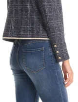 Chaqueta de tejido tweed en tono azul con sutiles destellos de lúrex. Presenta cuello a la base, abertura frontal y bolsillos decorativos. Las mangas largas incluyen detalle de botones metálicos dorados en los puños, y cuenta con vivos a contratono en los bordes.