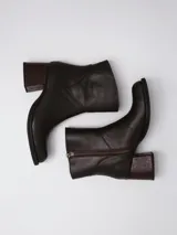 Botas de caña baja en cuero color marrón oscuro, con taco cuadrado y punta redondeada. Presentan un diseño tipo western con estribo desmontable que incluye una hebilla metálica decorativa.