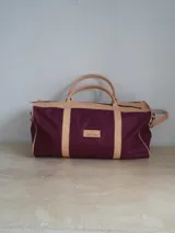 Bolso de lona color verde militar con detalles en cuero marrón. Tiene doble asa de mano y correa de hombro ajustable y extraíble.