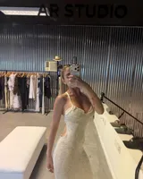 Vestido largo de tejido de punto blanco marfil, con escote halter anudado y aberturas pronunciadas en los laterales de la cintura. Presenta un tajo en la falda.