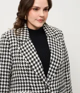 Blazer de sastrería confeccionado en tejido tweed con estampado pied de poule en blanco y negro. Presenta cuello con solapa, cierre frontal con un botón, mangas largas y bolsillos frontales con solapa.