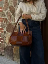 Cartera de hombro confeccionada en cuero y gamuza con diseño de damero, combinando paneles de texturas lisas y aterciopeladas. Presenta una manija trenzada y detalles de costuras artesanales en los laterales.