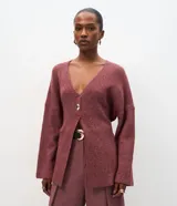 Cardigan de tricot en color borravino, con textura acanalada, escote en V profundo y cierre frontal con un único botón metalizado. Presenta mangas largas y un diseño alargado con amarre ajustable en la espalda.