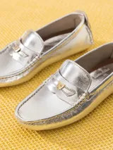 Mocasín de cuero vacuno con acabado metalizado plateado y textura tipo crocco. Presenta un aplique metálico en forma de corazón sobre el frente y suela de goma con tacos.
