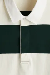 Remera tipo polo de manga larga con diseño de rayas horizontales anchas en color verde oscuro y blanco. Presenta cuello inglés en contraste, tapeta con botones ocultos y puños acanalados.