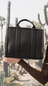 Cartera estructurada de tamaño mediano, confeccionada en símil cuero color negro. Presenta doble asa de mano, correa larga ajustable y desmontable, y un bolsillo trasero con cierre. El compartimento principal cuenta con cierre, división interna y bolsillos organizadores.
