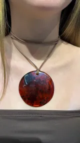 Gargantilla tipo choker con cordón de gamuza marrón y dije circular grande de resina en tonos rojizos y oscuros con efecto marmoleado.