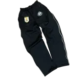 Campera deportiva negra con capucha, cierre frontal metálico y detalles de ribetes blancos. Presenta un escudo bordado en el pecho con motivos uruguayos y un logo reflectivo circular en el lado opuesto. Cuenta con bolsillos laterales con cierre.