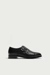 Zapato de vestir tipo monk de color negro, con detalle de doble hebilla metálica plateada en el empeine, puntera redondeada y suela con ligero tacón.