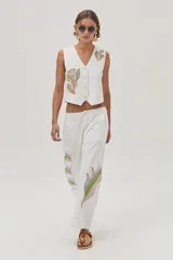 Chaleco blanco de gabardina con bordados florales y cierre frontal con botones forrados en la misma tela.