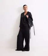 Pantalón wide leg de cintura alta, confeccionado en tejido satinado color negro, con elástico y lazo en la cintura y bolsillos delanteros.