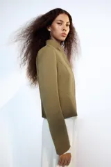 Cazadora entallada Zara color verde militar, con cuello alto, manga larga y bajo acabado en peplum. Cuenta con cierre frontal oculto con cremallera y botones a presión.