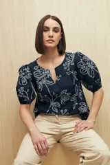 Blusa azul marino con bordados calados en color blanco. Presenta escote en pico, mangas abullonadas con puños elásticos y un diseño de ajuste relajado.