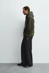 Sudadera de corte relajado confeccionada en tejido técnico con elasticidad y efecto neopreno. Presenta capucha ajustable con cordones, cierre frontal de cremallera de doble dirección, bolsillos tipo canguro y terminaciones en rib.