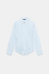 Camisa de popelín color celeste, con cuello solapa, manga larga y cintura entallada con pliegues. Presenta cierre frontal con botones ocultos por solapa.