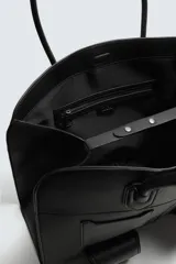 Bolso de viaje negro con acabado grabado y diseño de múltiples bolsillos frontales. Dispone de un compartimento principal con cierre magnético, un bolsillo interno con cremallera y tres bolsillos exteriores de diversos tamaños con cierre de imán. Incluye dos asas de mano superiores.