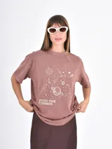 Remera de algodón color marrón con efecto lavado, cuello redondo y manga corta. Presenta un estampado frontal con temática espacial que incluye planetas, estrellas y la frase 'Into the cosmos'.