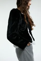 Chaqueta corta de piel sintética en color negro, con cuello redondo, hombreras marcadas y cierre frontal oculto.