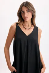 Vestido largo negro sin mangas, con escote en V, pinzas frontales, bolsillos laterales y caída fluida.