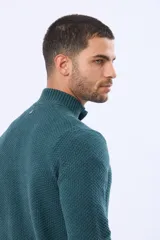 Buzo tejido texturado color verde oscuro, con cuello alto y cierre parcial de tres botones. Tiene mangas largas y un pequeño detalle de etiqueta marrón en el dobladillo inferior.