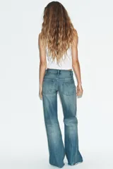 Jeans de tiro medio con diseño flare, efecto lavado y detalles de roturas en las piernas. Presenta cinco bolsillos, trabillas para cinturón y bajo deshilachado sin costuras.