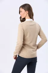 Buzo tejido en hilo de algodón color beige, con cuello redondo y manga larga. Presenta un corte clásico y un pequeño detalle metálico en la parte inferior izquierda.