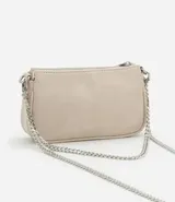 Cartera femenina modelo baguette, color beige, con acabado brillante y asas desmontables. Confeccionada en poliuretano, tiene una correa de cadena plateada y un logo metálico en el frente.