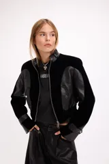 Campera crop de paño negro con recortes en cuero sintético, cuello alto con hebilla metálica, cierre frontal y hombreras marcadas.