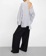 Camisa de algodón a rayas blancas y azules con diseño desestructurado, cuello italiano, manga larga y cierre de botones. Cuenta con una pieza asimétrica multiposición en la parte frontal.