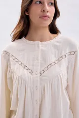 Blusa de estilo romántico en color crudo, confeccionada en tela texturizada con detalles de encaje y alforzas en el canesú. Presenta cuello redondo, cierre frontal con botones y mangas largas con puños delicados.