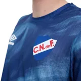 Remera de fútbol Umbro del Club Nacional de Football modelo Press, con diseño estampado abstracto en tonos rojo y azul, cuello redondo y mangas cortas. Cuenta con el logo de Umbro y el escudo del club bordados en el pecho.