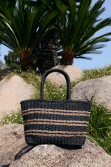 Bolso tipo tote negro tejido con rayas horizontales en color tostado, asas de mano rígidas y diseño estructurado.
