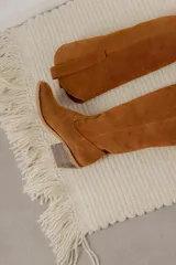 Bota estilo tejana de caña alta, confeccionada en gamuza, con taco cuadrado y diseño de costuras decorativas.