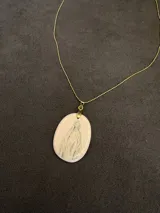 Collar de cadena fina dorada con dije ovalado de cerámica en tono crema, ilustrado con la figura de la Virgen.