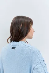 Sweater de punto color celeste, con diseño de trenzas y detalles de cordones entrelazados en el frente y las mangas. Presenta cuello redondo y puños acanalados.