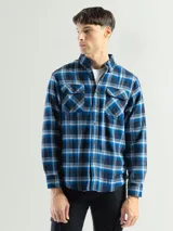 Camisa de franela a cuadros color celeste, gris y negro, de manga larga con dos bolsillos frontales con solapa abotonada.