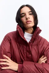 Campera puffer de corte cropped, color marrón oscuro, con cuello alto, cierre frontal con cremallera y botones a presión, y puños elásticos.