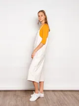 Mono de jean color crudo, de corte holgado, con pierna ancha y largo cropped. Tiene tirantes finos y un bolsillo cuadrado en el pecho.