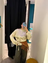 Cinto de cuero negro con diseño asimétrico, decorado con tachas metálicas doradas y flecos largos en el borde inferior.